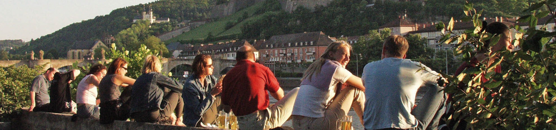 Menschen am Main mit Blick auf die alte Mainbrücke, das Käppele und die Festung Marienberg.